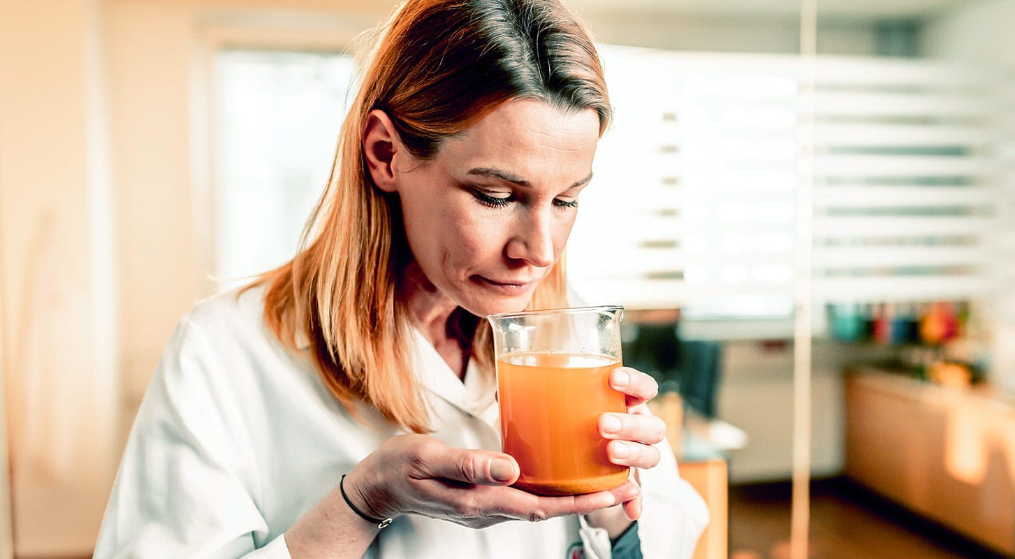A woman smiles while holding a glass of turmeric tea in her hand.